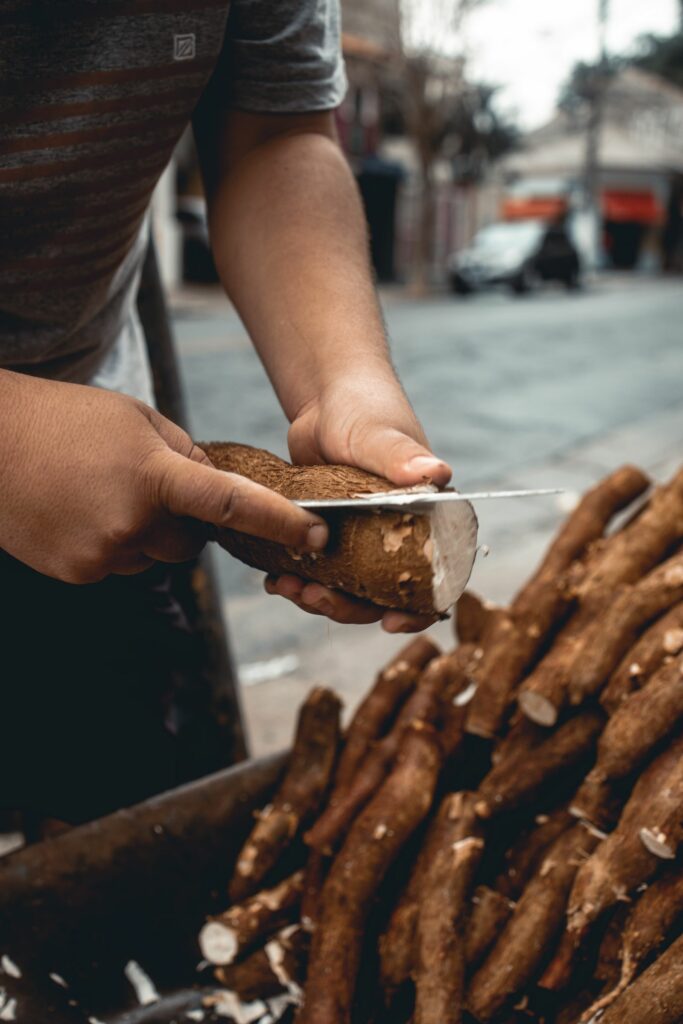 Mains épluchant une racine de manioc devant un tas de tubercules frais